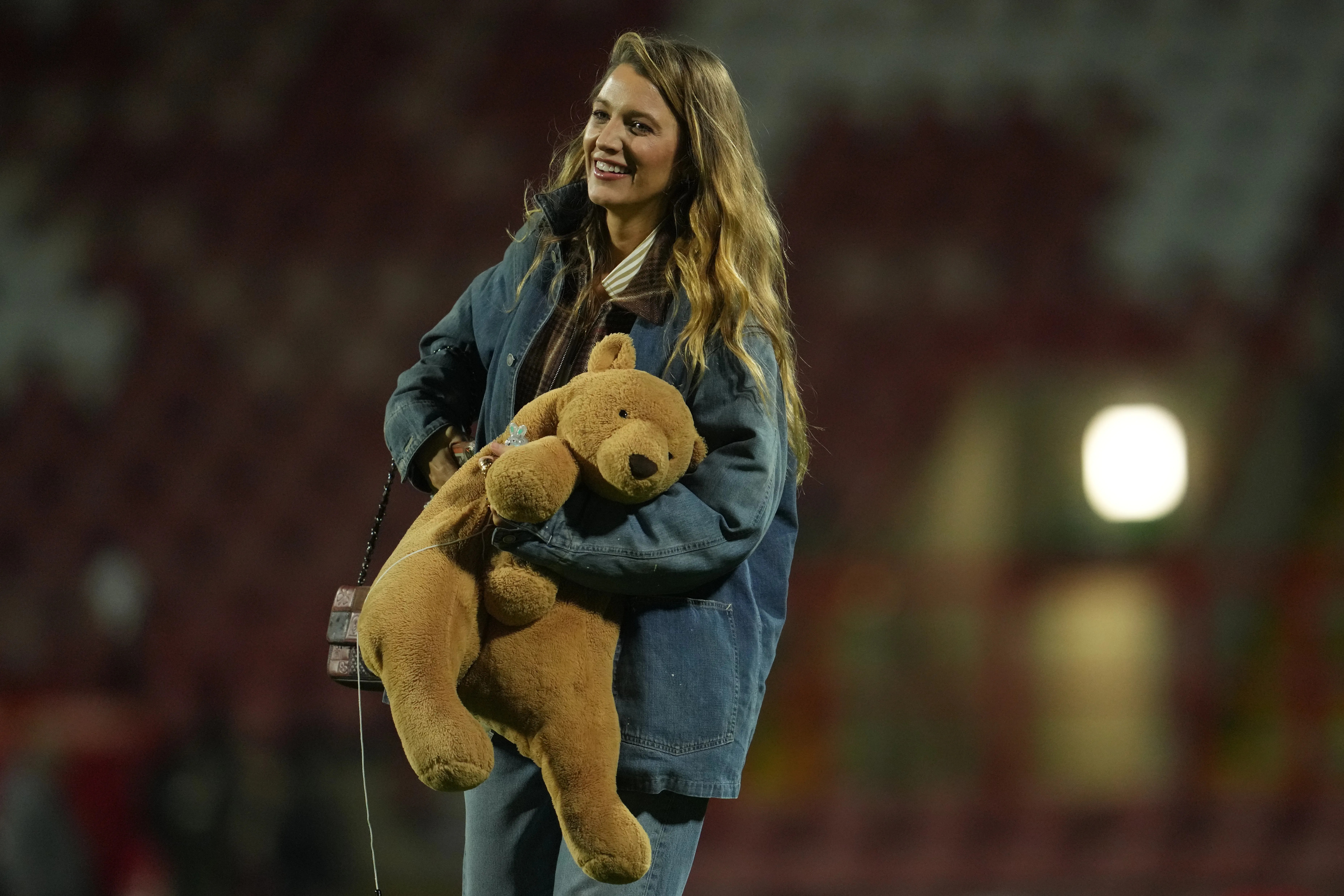 Blake Lively walks on the pitch after a soccer match holding a large teddy bear.