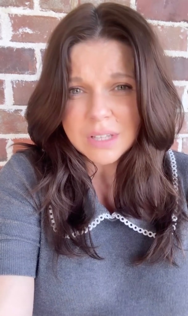 Amy Duggar with a concerned expression, wearing a gray top with white scalloped trim.
