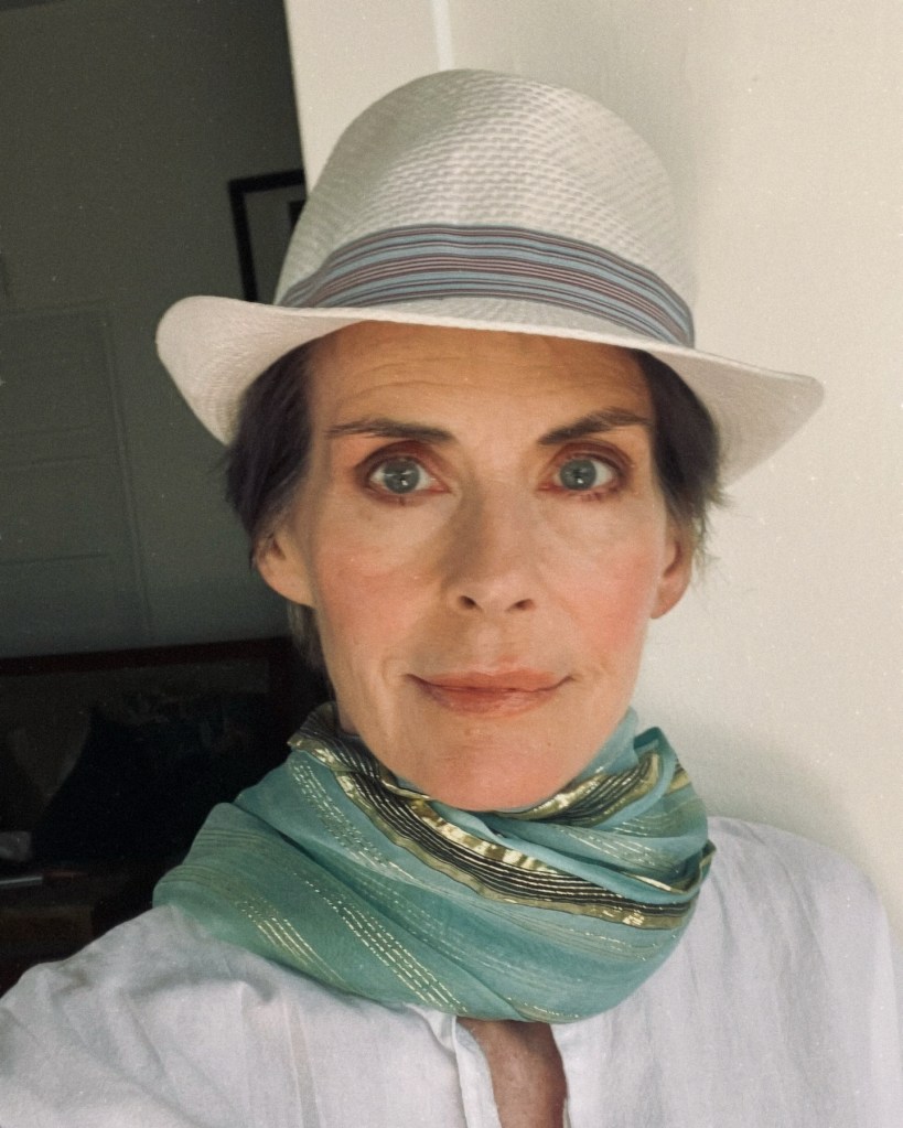 Annabel Schofield wearing a white fedora hat and a teal scarf.