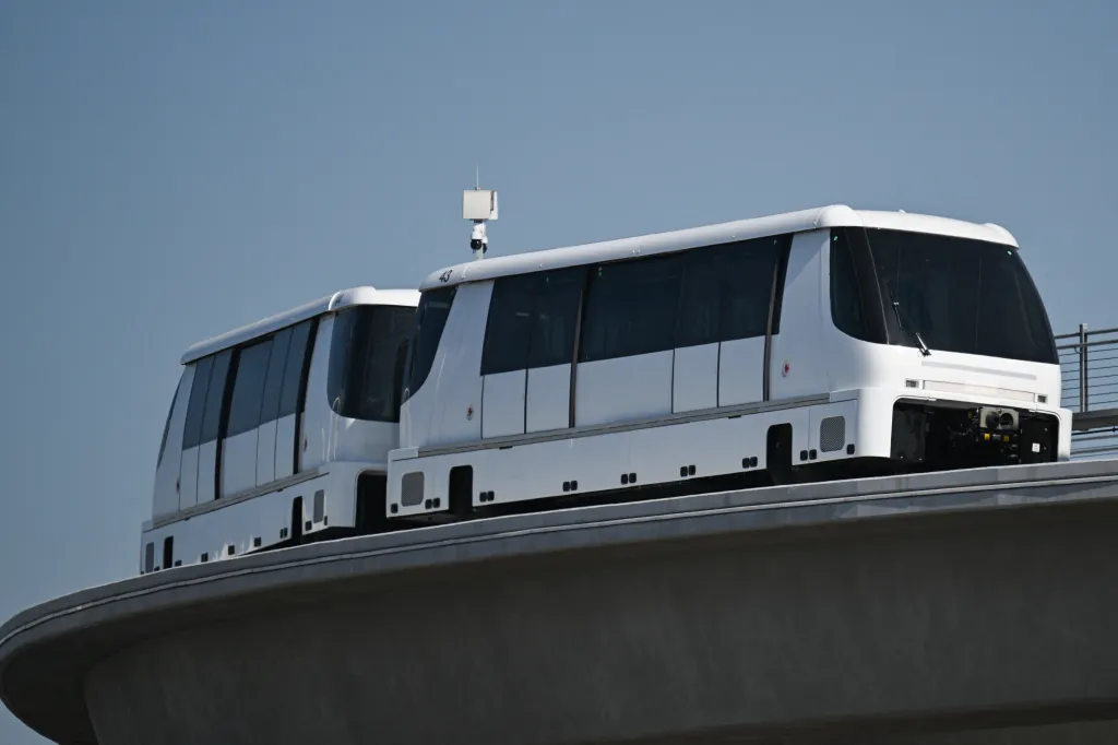 Two white APM train cars on a raised track at LAX.