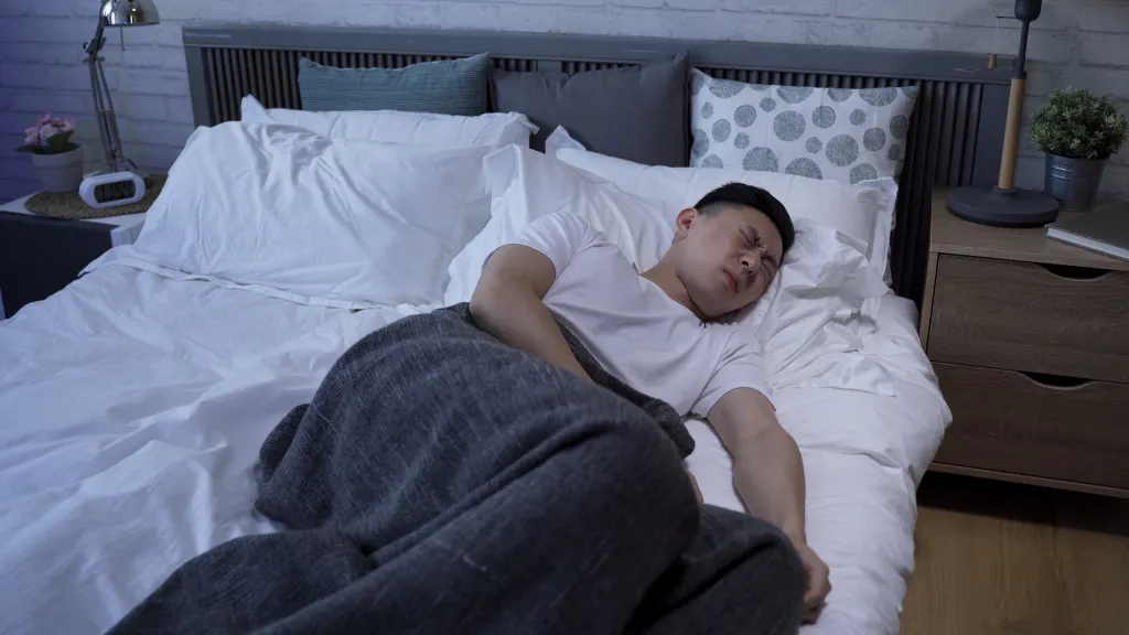 A man in bed, distressed, tossing and turning, suffering from a disturbed sleep.