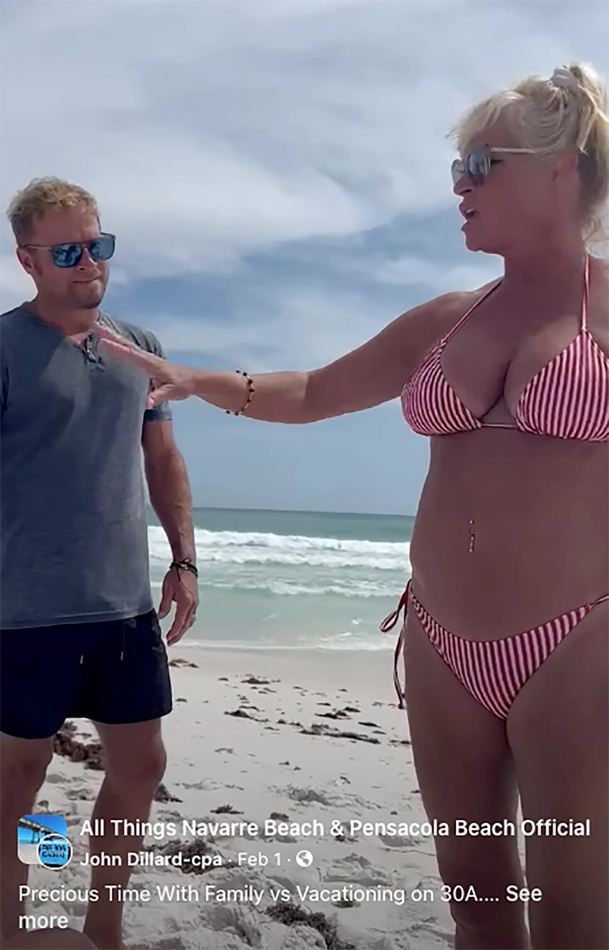 A woman in a red and white striped bikini gestures at a man wearing sunglasses and a grey shirt on a beach.