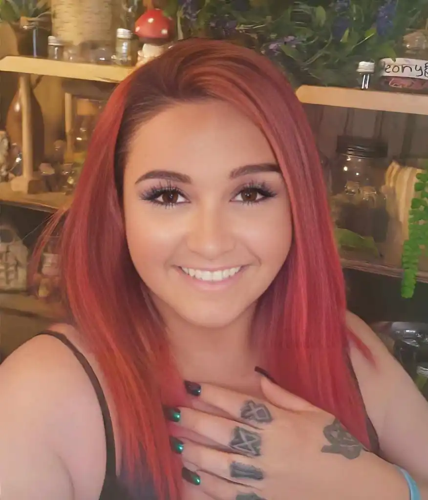 Rowan MacKenzie, a doomsday prepper, smiling with red hair, green painted fingernails, and tattoos on her fingers and hand.