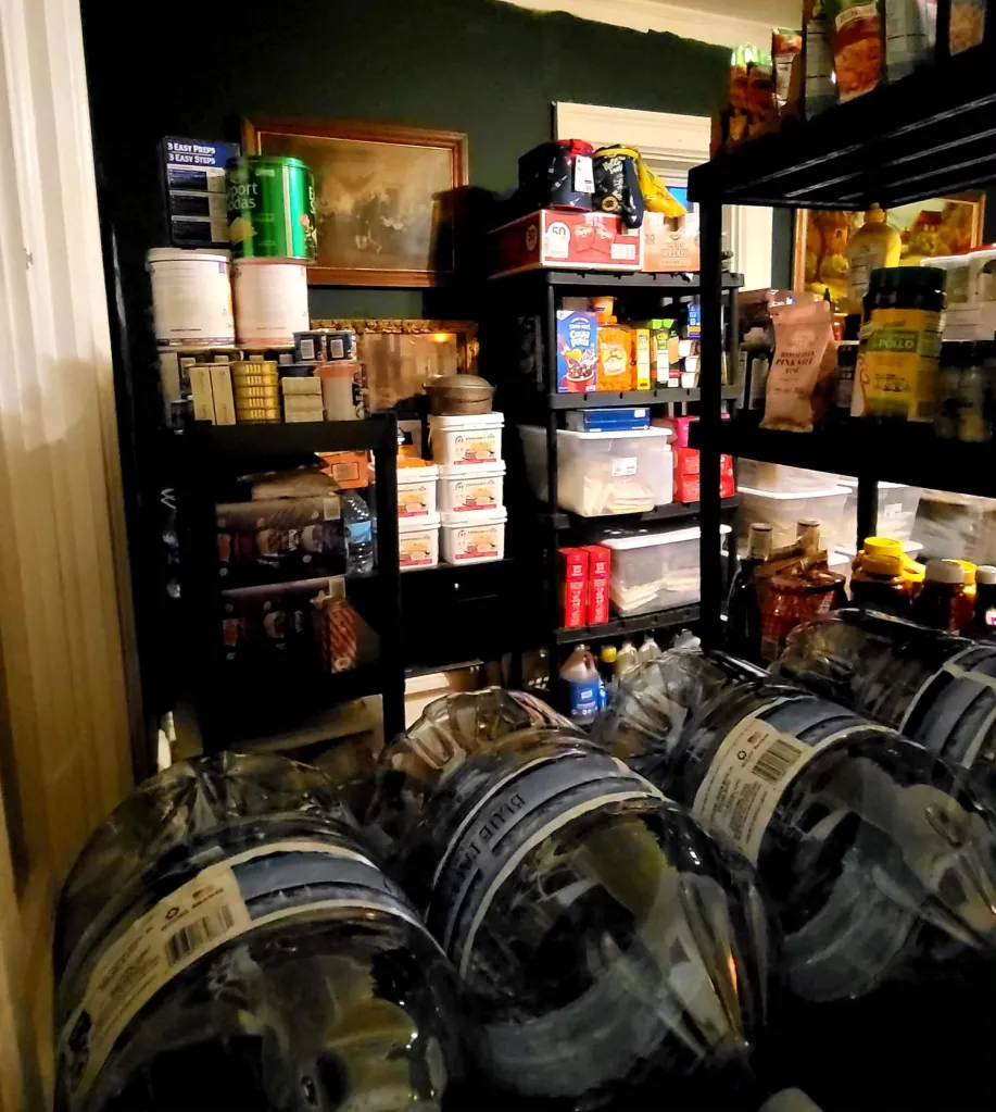A storage room filled with shelves of non-perishable food, water jugs, and other supplies, prepared by a doomsday prepper.