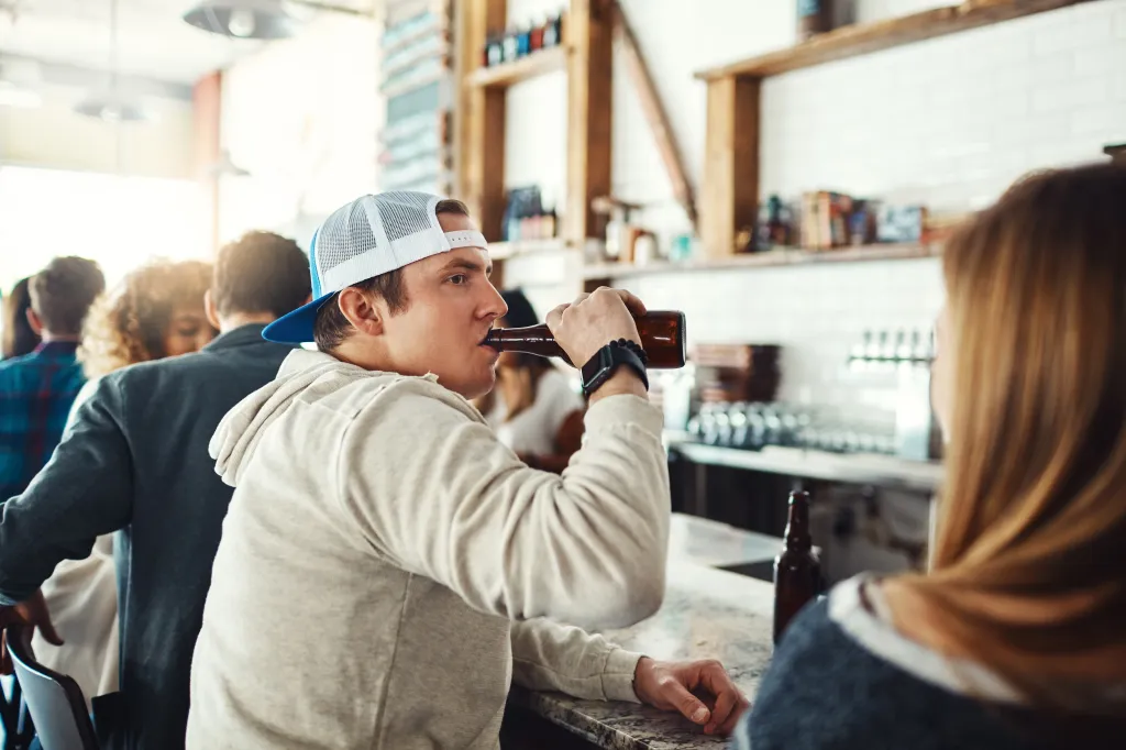 Man in a baseball cap drinking beer at a bar.