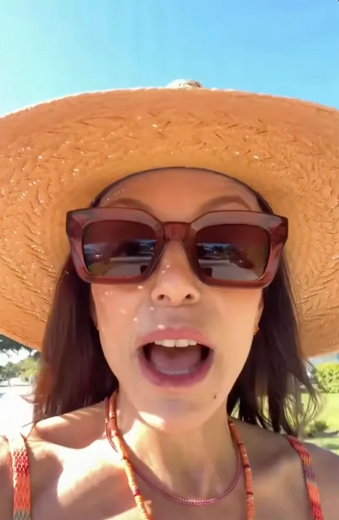 Bethenny Frankel wearing a straw hat, sunglasses, and an orange top.