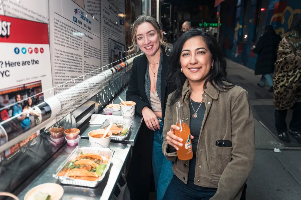 Julie Ferguson and Veronica smiling and posing with tacos and a drink from Birria-Landia taco truck.