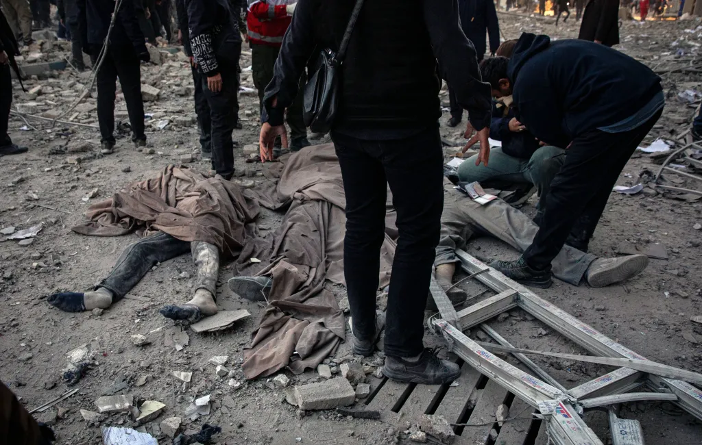 Two bodies covered in cloth on a debris-strewn street after a strike in Tehran, Iran.