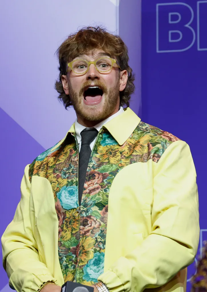 West Wilson at BravoCon, wearing a yellow jacket with a floral print and yellow glasses, mouth open.