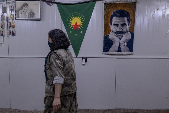 A woman in military fatigues walks past a poster of Abdullah Ocalan, the jailed founder of the Kurdistan Workers’ Party (PKK)