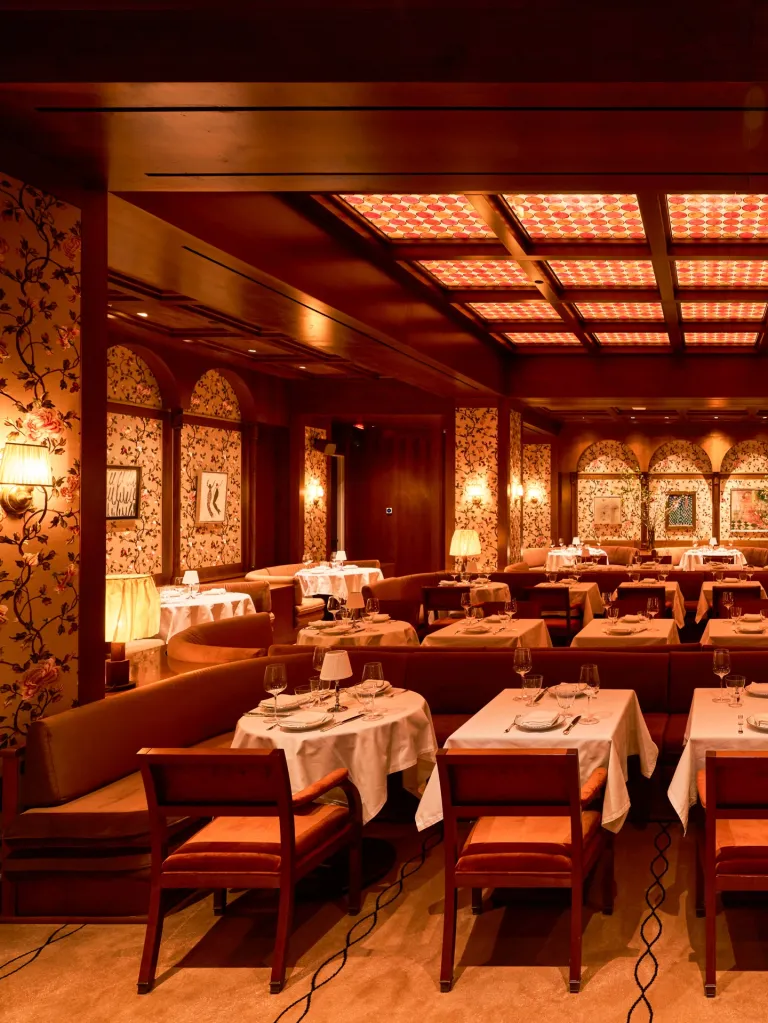 An empty restaurant dining room with banquettes and tables set with white tablecloths and glassware.