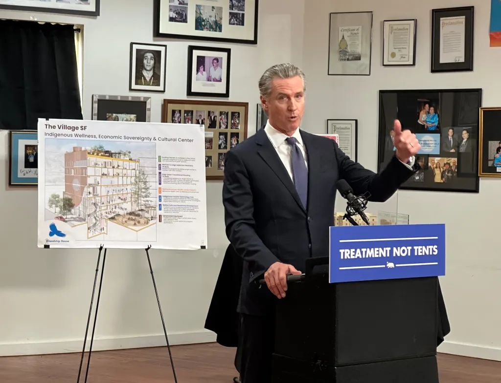Gavin Newsom speaking at a podium with a sign that says 