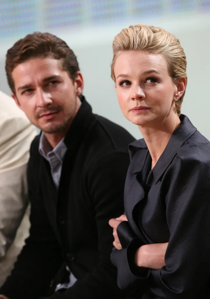 Shia LaBeouf, in a black jacket and blue shirt and Carey Mulligan, in a black shirt, attend a TV program.