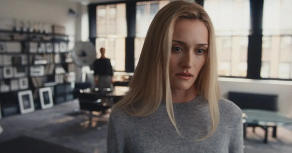 Woman with long blonde hair looking down while wearing a gray sweater.