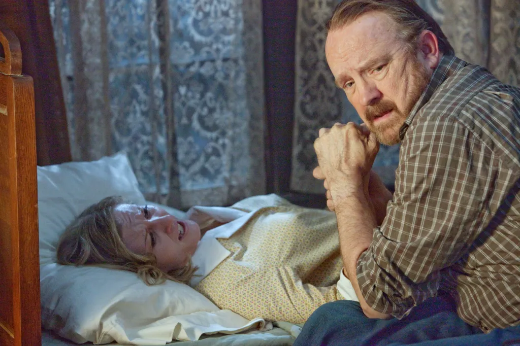 Jim Beaver kneels by Carrie Anne Fleming who is lying upset on a bed.