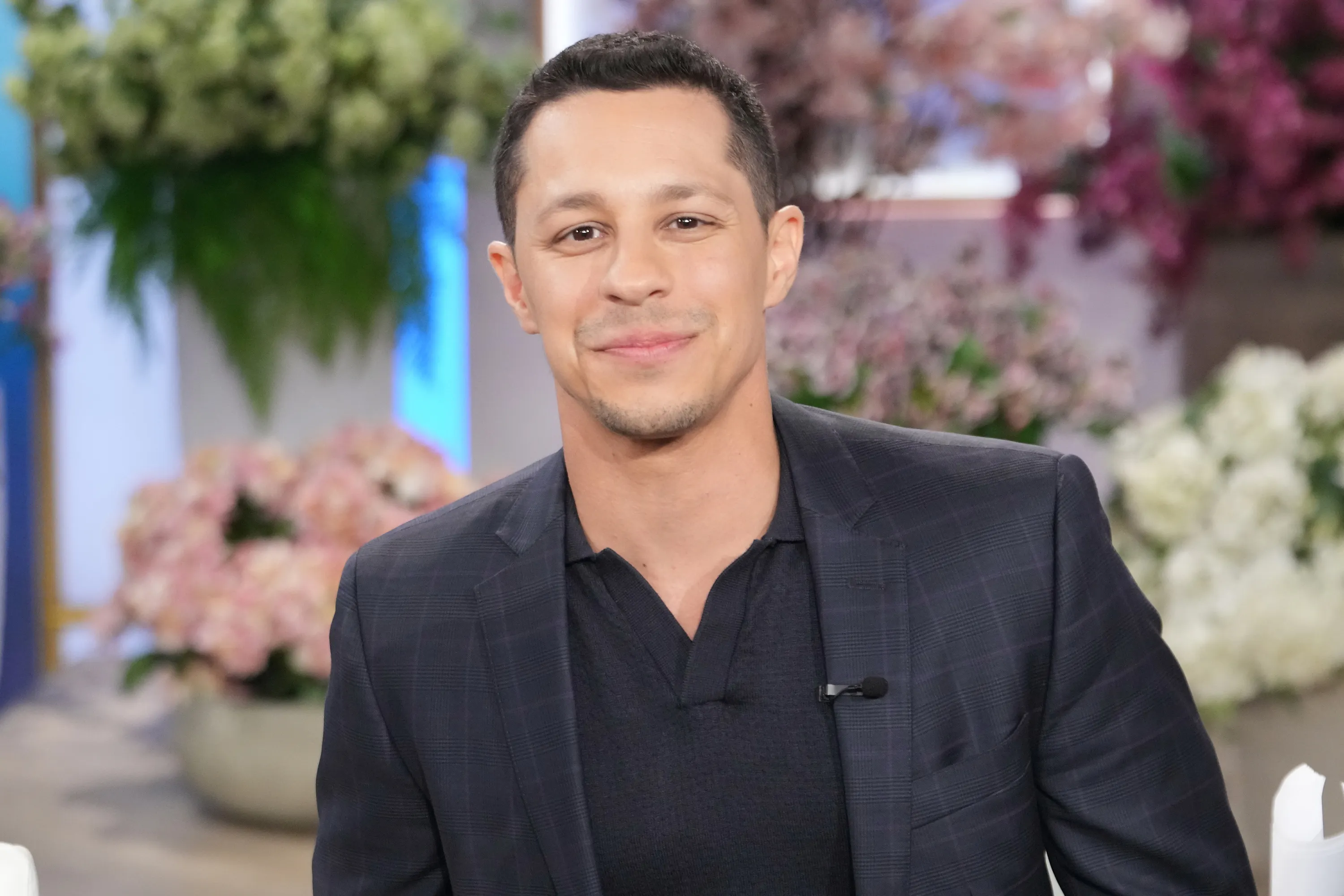 David Del Rio smiling while wearing a dark plaid suit jacket over a dark shirt.