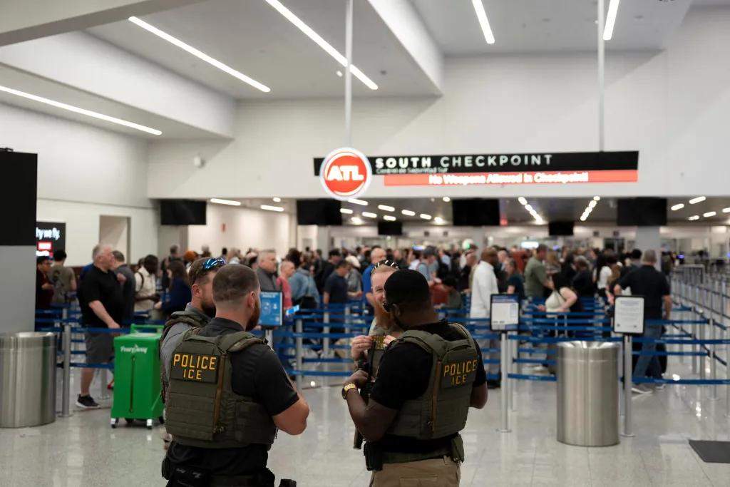 ICE agents in tactical vests talk at an airport security checkpoint.