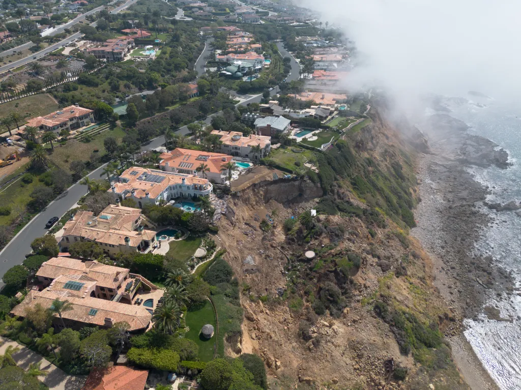Aerial view of houses on a cliff in Palos Verdes with a landslide impacting properties and the ocean to the right partially obscured by fog.