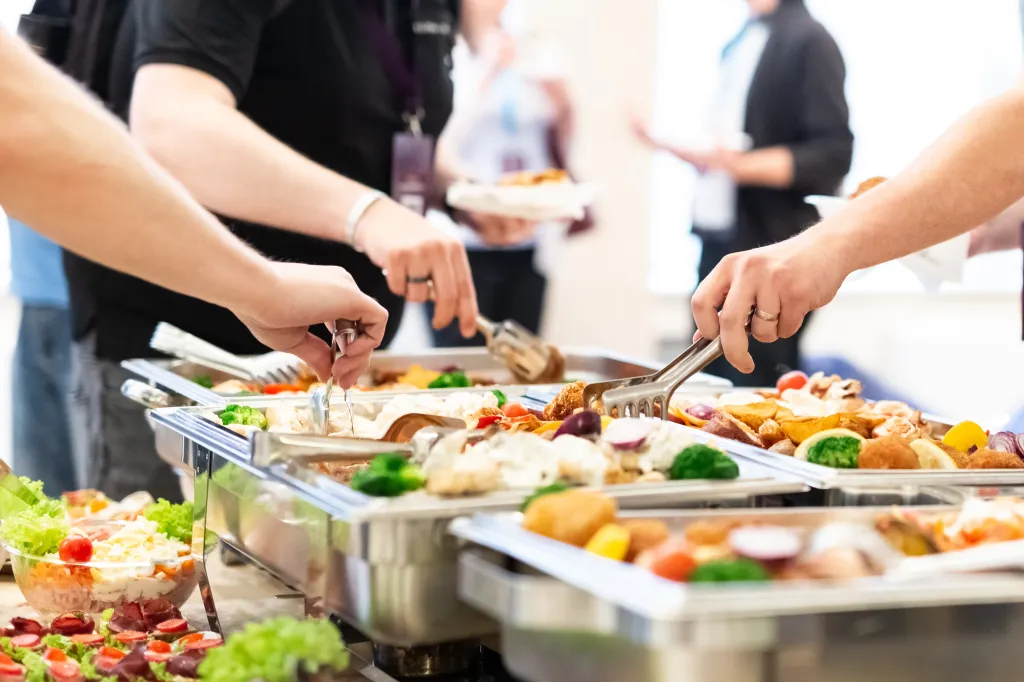 Hands using tongs to serve food from a buffet.