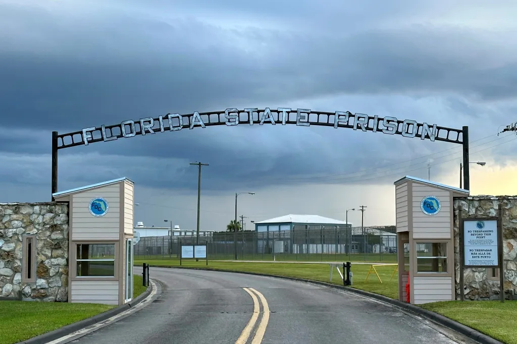 Entrance to Florida State Prison with a sign arching over the road and guardhouses on either side.