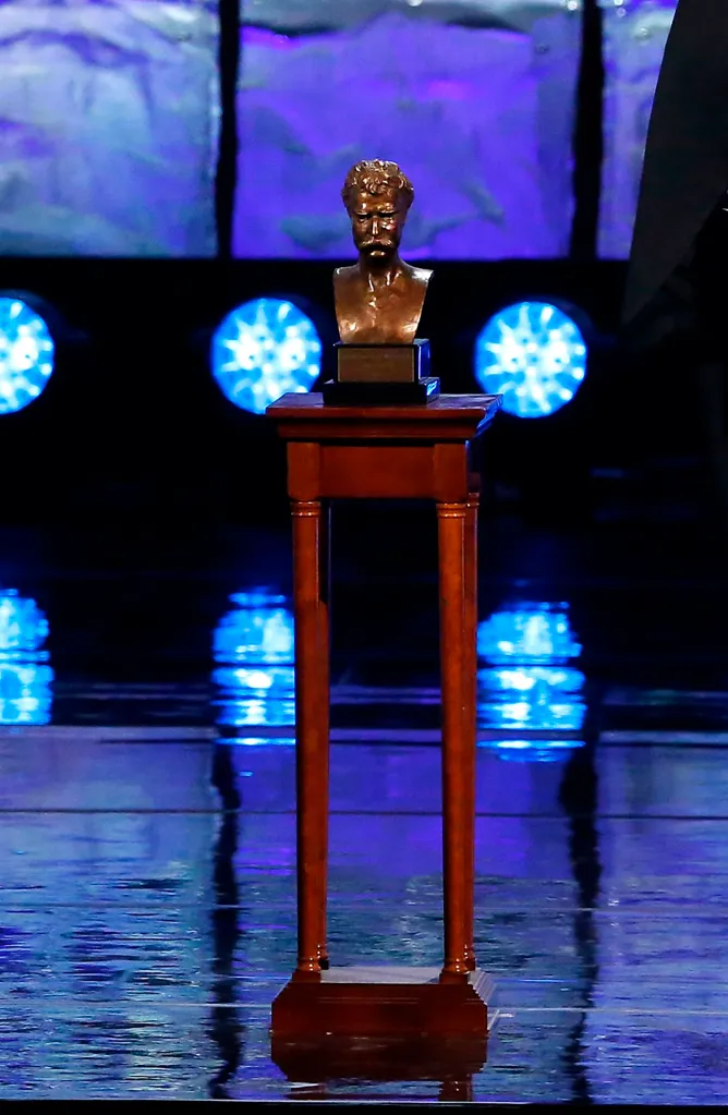 A bronze bust of Mark Twain on a wooden pedestal, illuminated by blue stage lights.