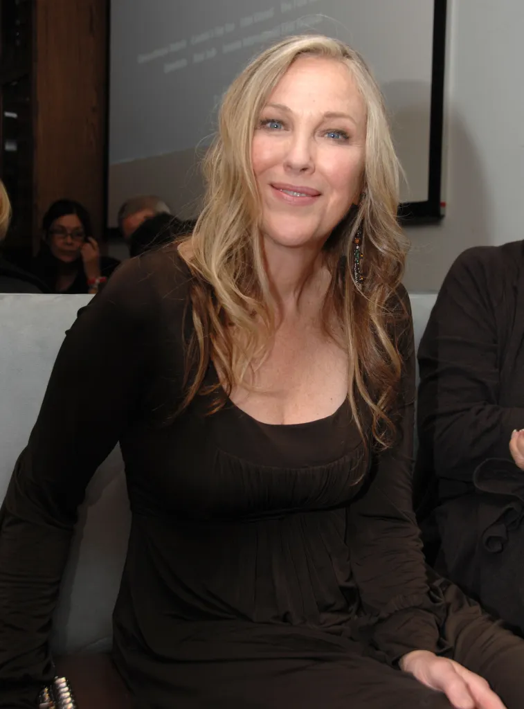 Catherine O'Hara smiles while wearing a dark brown long-sleeved dress.