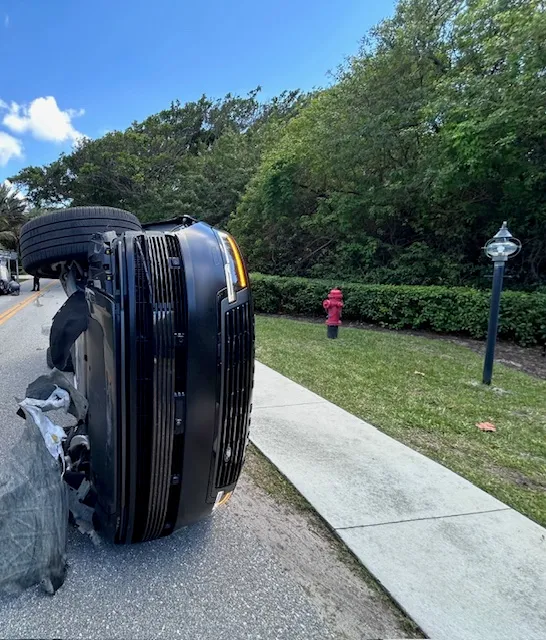 An overturned SUV on a road, with a red fire hydrant and trees in the background.