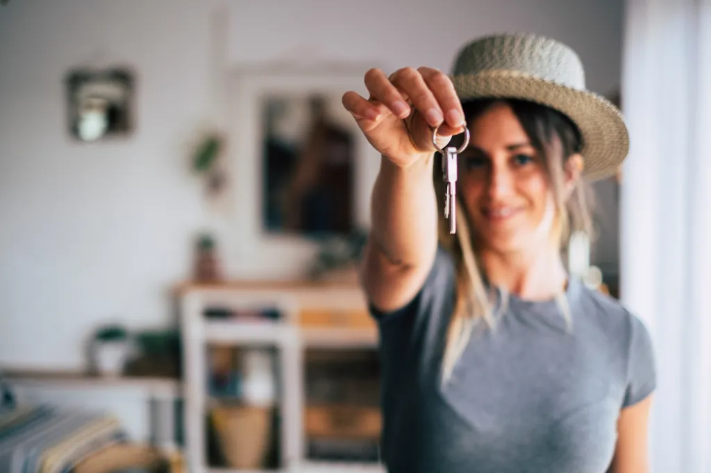 A young woman in a straw hat holds up a new house key.