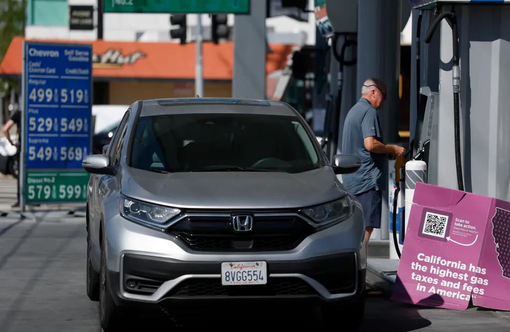 A man pumps gas into his car at a Chevron station where prices are over $5 a gallon, with a sign in front stating 