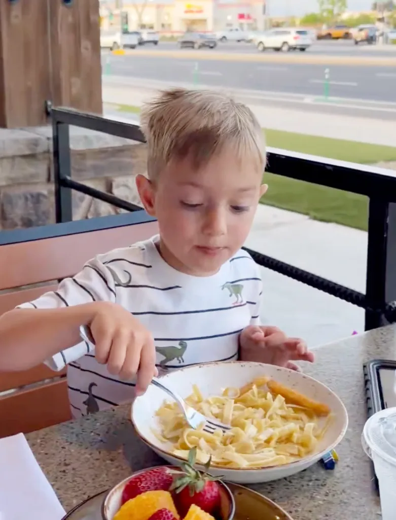 Young boy eating pasta at an outdoor restaurant.