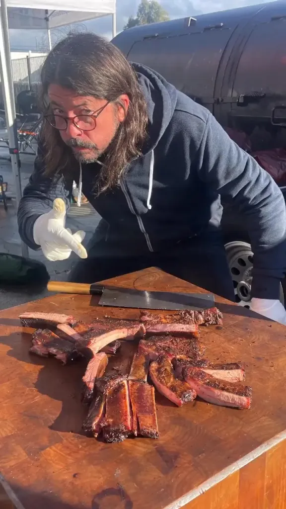 Dave Grohl pointing at a platter of ribs he prepared.
