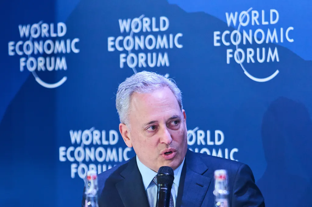 A man with gray hair and a blue suit speaking into a microphone with 