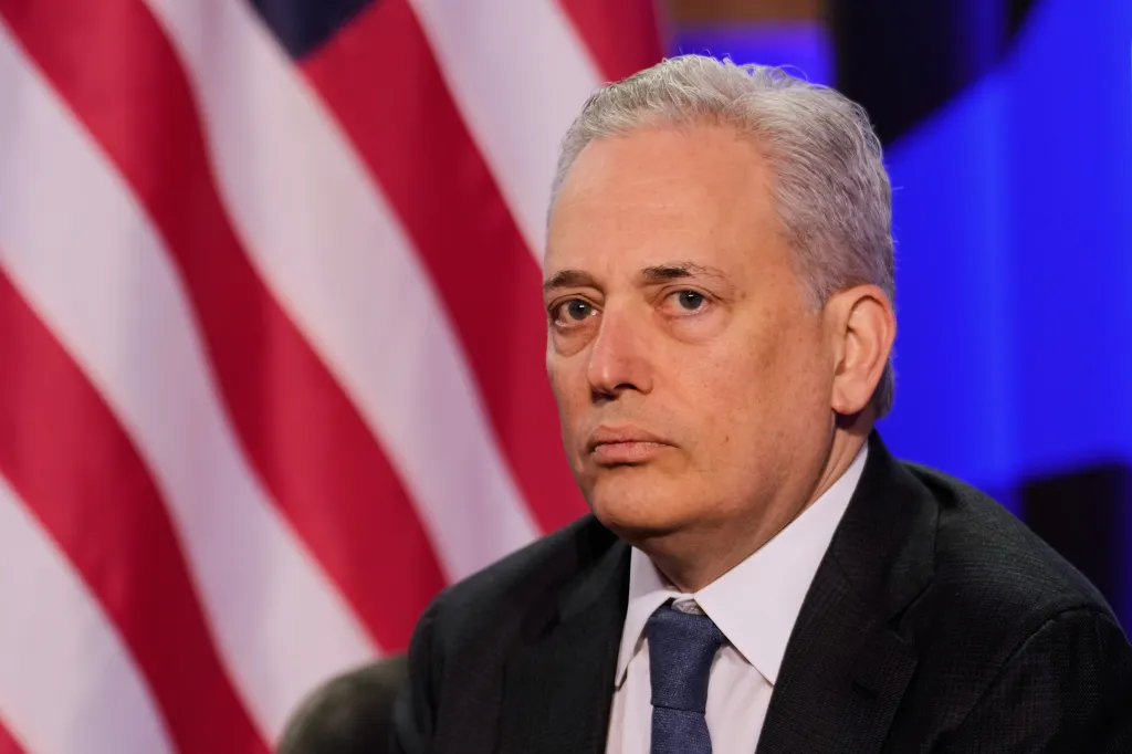 David Sacks looking off-camera against a backdrop of the American flag.