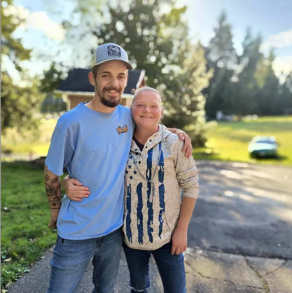 A young man with a beard and a woman with her hair pulled back, standing with their arms around each other.
