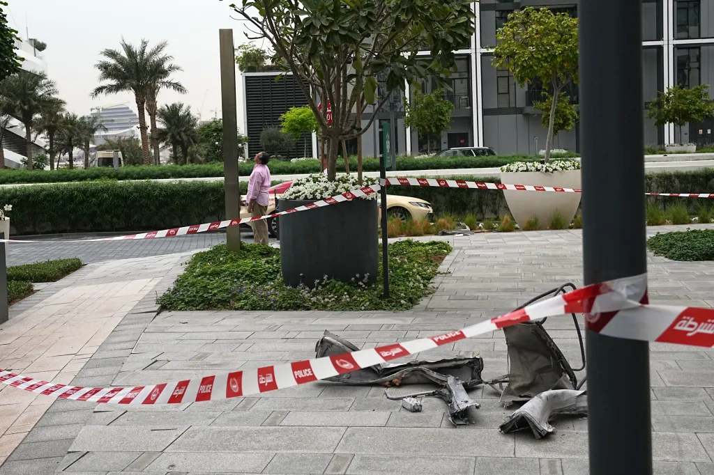 Debris from a drone strike on the sidewalk at the Address Creek Harbour hotel in Dubai, with police tape marking off the area.