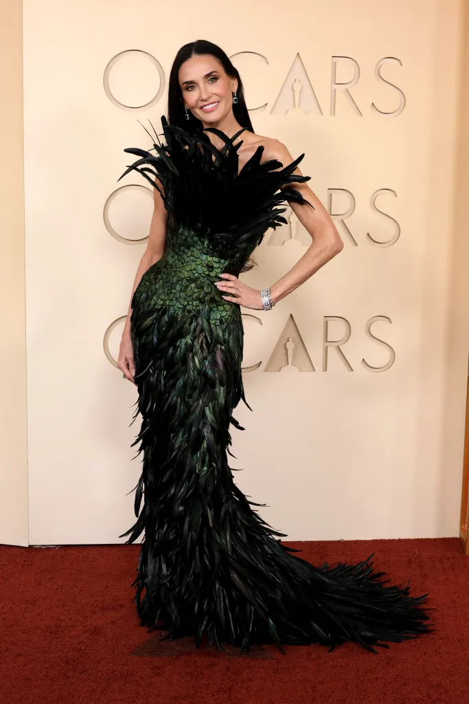 Demi Moore in a strapless green and black feather gown poses at the Oscars.