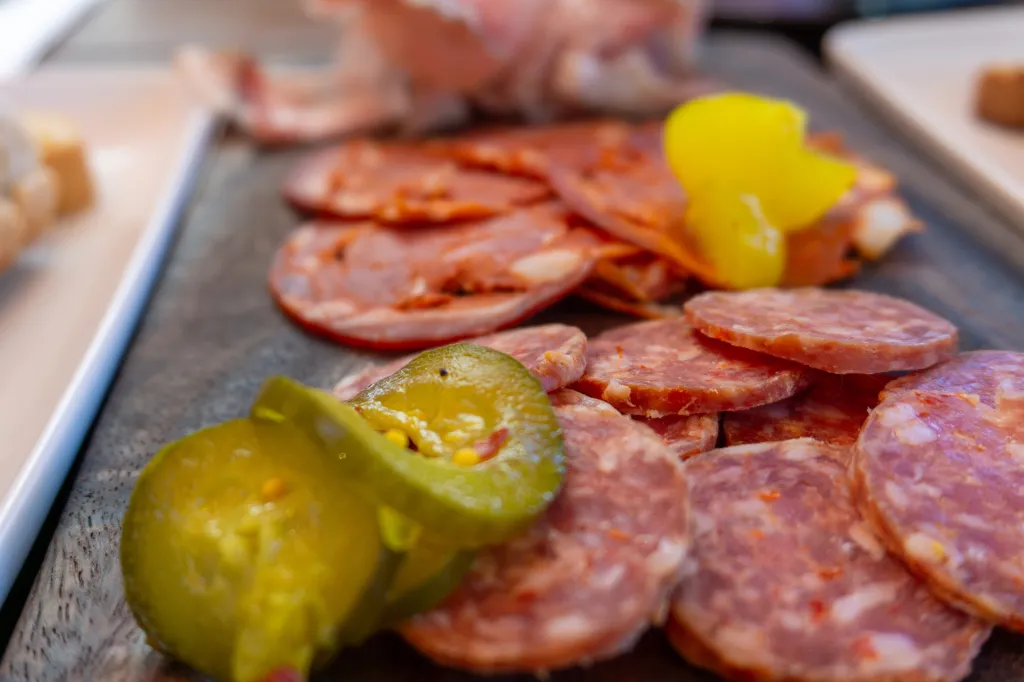 Sliced salami and pickles on a wooden board.