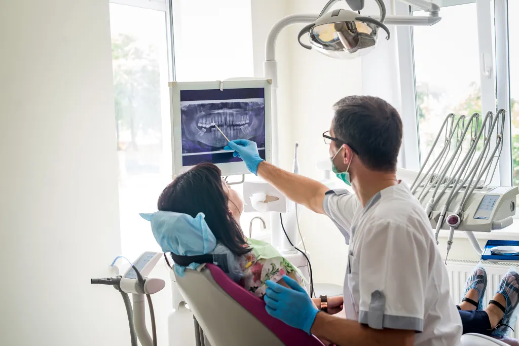 Dentist showing a patient an X-ray of their teeth on a screen.