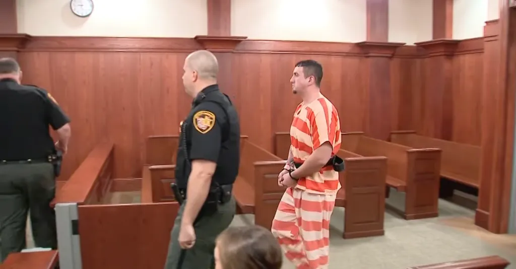 Kyle Long, a man in an orange and white striped jumpsuit, is escorted by two officers in a courtroom.
