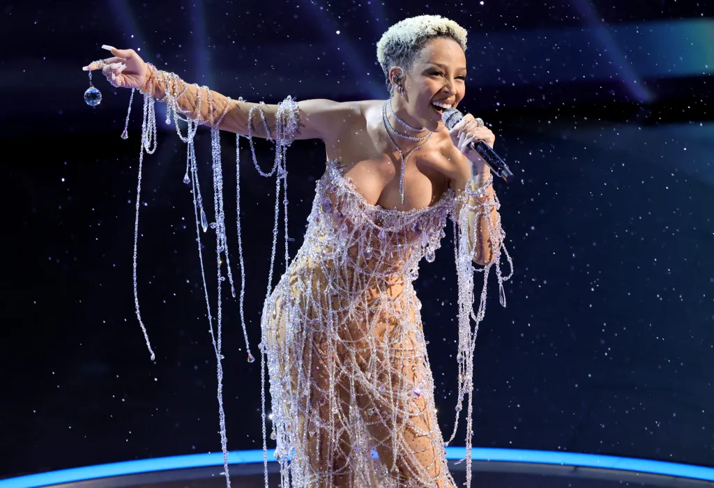 Doja Cat singing while wearing a sparkling outfit with dangling crystal beads.