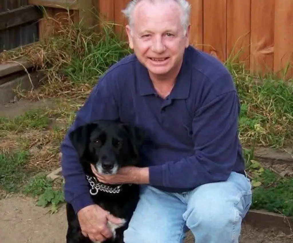 Donald Weynandt, an 81-year-old victim, kneeling and holding a black dog.