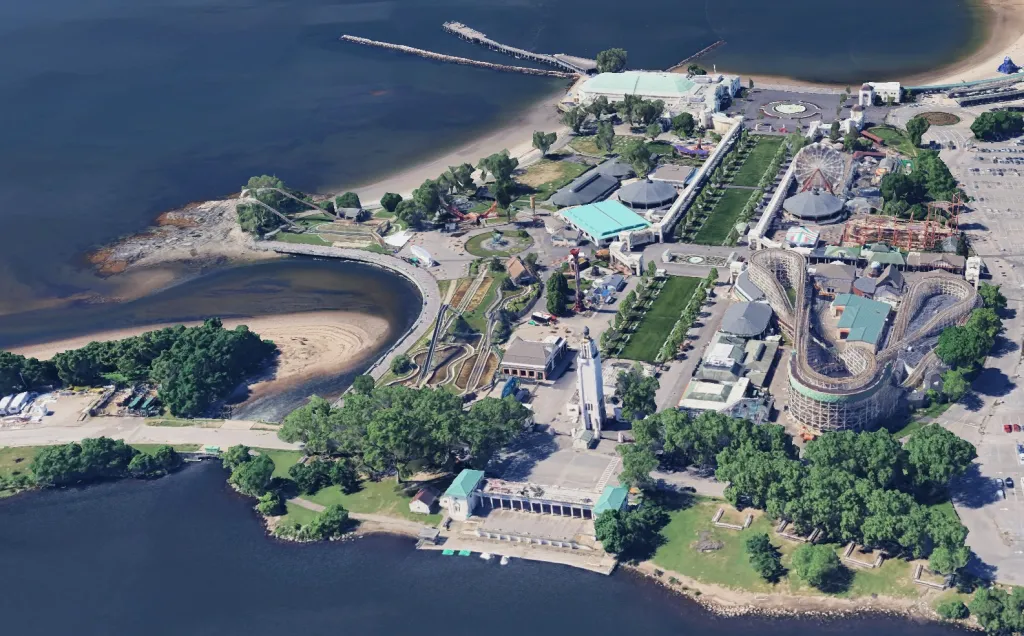 Aerial view of Rye Playland amusement park on the water, with a roller coaster, other rides, and a beach.