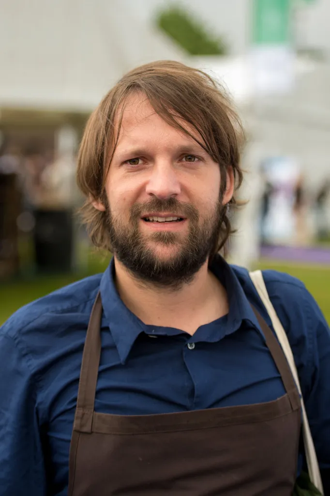 René Redzepi, chef and owner of Noma, wearing a blue shirt and brown apron.