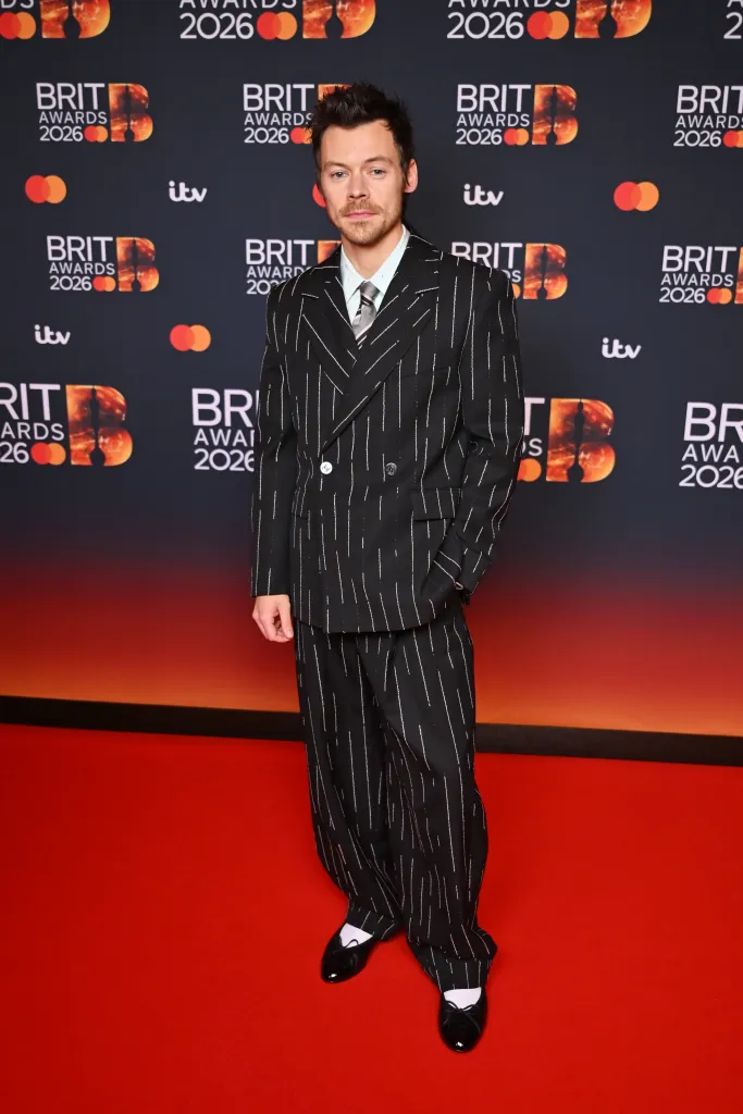 Harry Styles poses on a red carpet in a pinstriped suit at The BRIT Awards 2026.