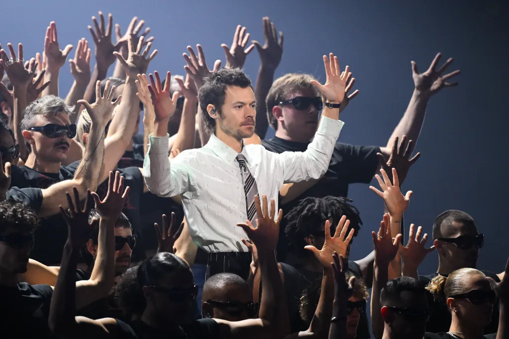 Harry Styles performing on stage surrounded by dancers with raised hands during The BRIT Awards.