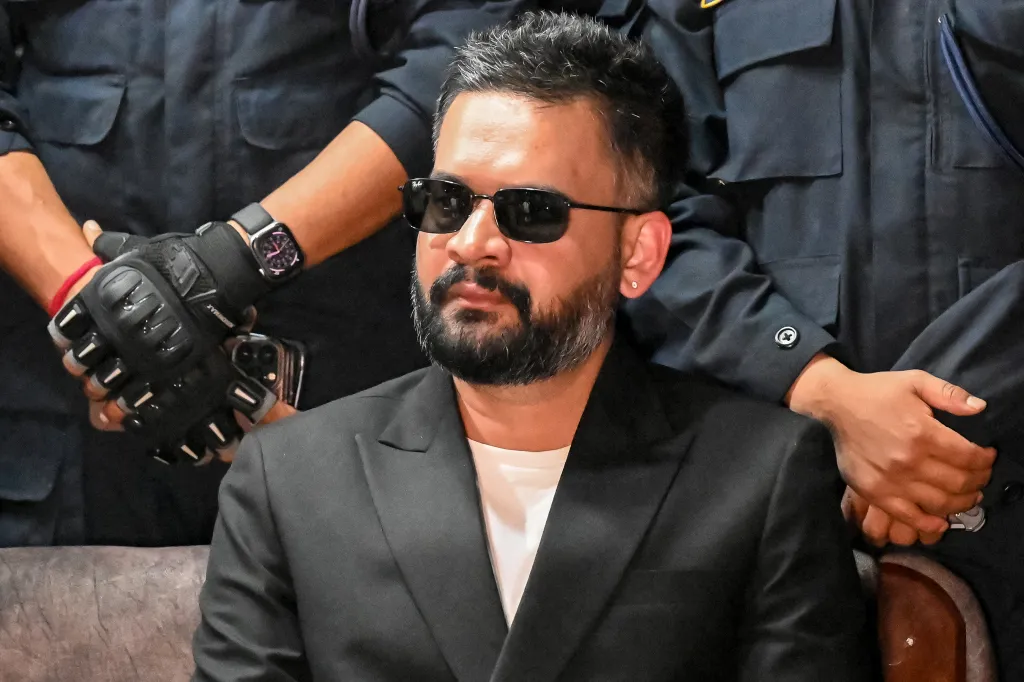 Rastriya Swatantra Party election candidate Balendra Shah in a black suit and sunglasses, with hands resting on his shoulders.