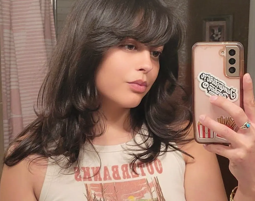 Emily Panuco taking a mirror selfie while holding a phone with stickers.