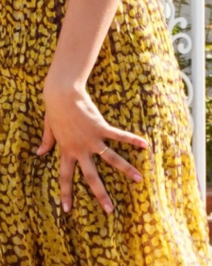 Zendaya's left hand with a gold band on her ring finger, against a yellow and brown patterned dress.