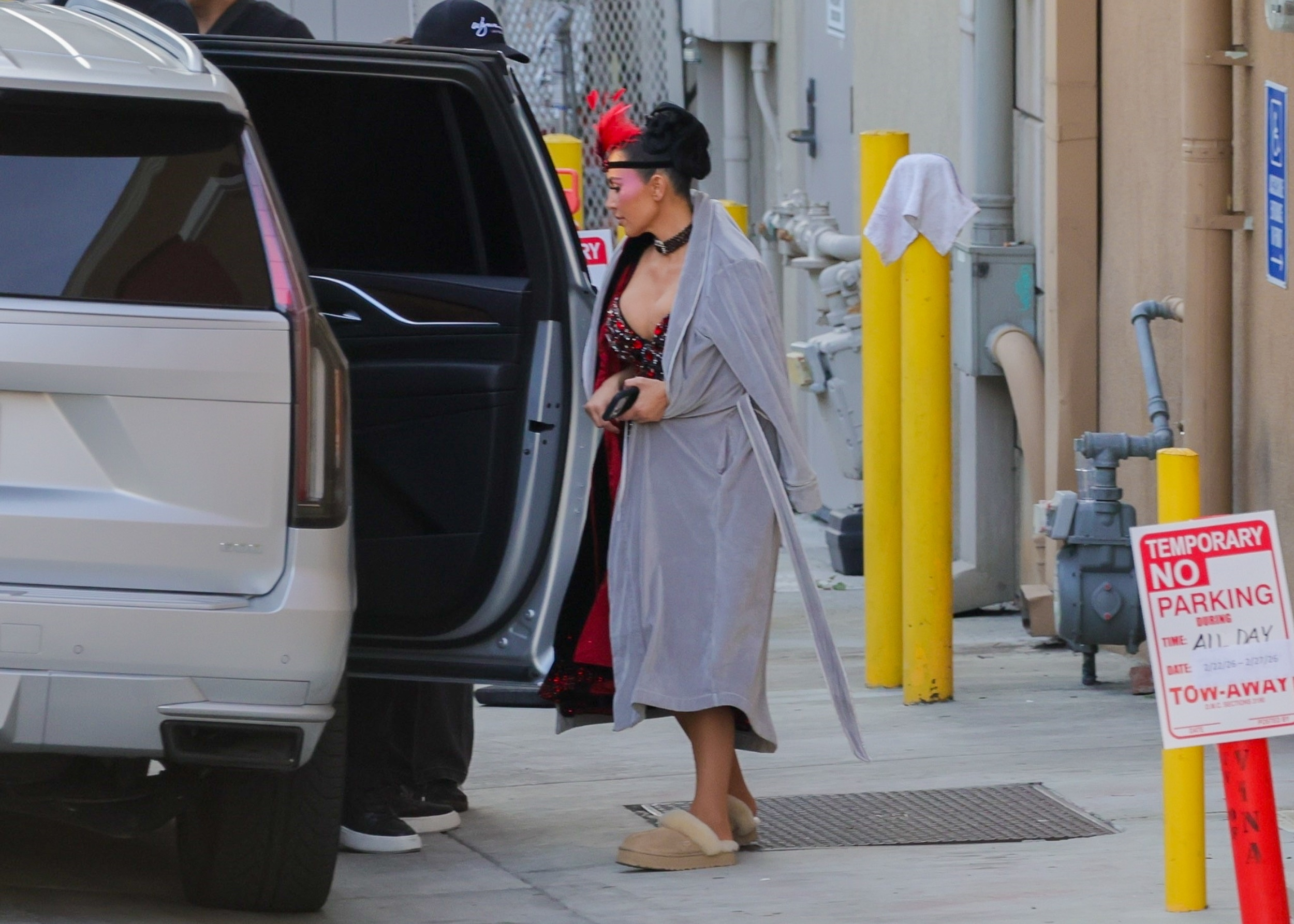 Kim Kardashian wearing a showgirl costume and a gray robe, exiting a white SUV on the set of 