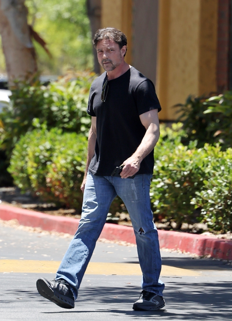Aaron Phypers walks, holding an iPhone, wearing a black t-shirt, jeans, and no wedding ring.